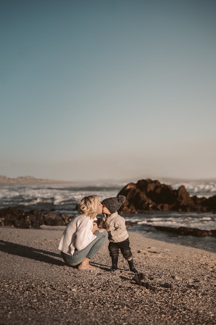 A touching scene of a mother and child sharing a kiss on a scenic beach during sunset.